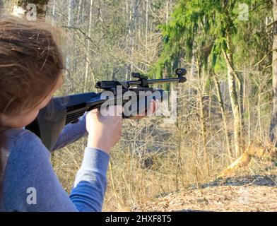 The girl shoots from an air rifle at a target in the forest. Stock Photo