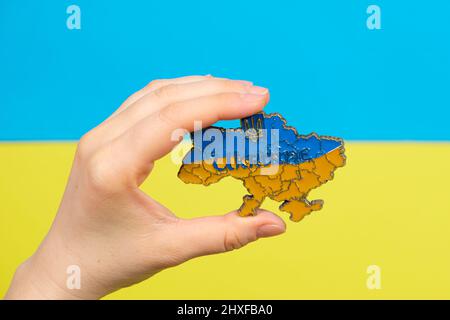 The map of Ukraine in the hand of a person on a blue yellow background - the color of the flag. Integrity and independence of Ukraine, war. Stock Photo
