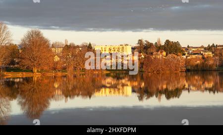 Sunset on a lake in Burgundy, France, with trees in winter and houses and buildings behind Stock Photo