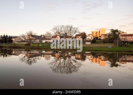 Sunset on a lake in Burgundy, France, with trees in winter and houses and buildings behind Stock Photo