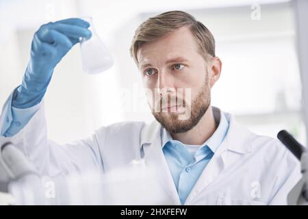 scientist is carefully looking at the liquid in the test tube. Stock Photo