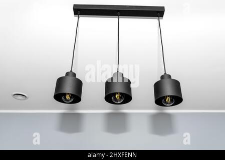 Modern chandeliers with tube shaped LED bulbs, covered with matt black paint, three bulbs visible. Stock Photo