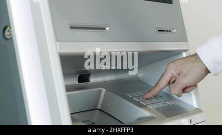 Male hand attaching card to the ATM bank machine for performing financial transactions. HDR. Close up of man entering bank card pin code. Stock Photo