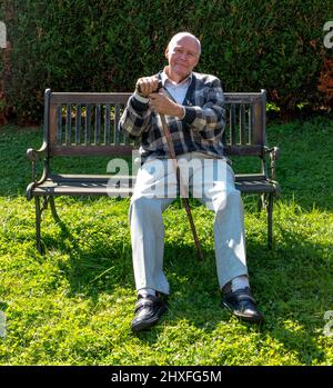 old man enjoys sitting on a bench in his garden Stock Photo