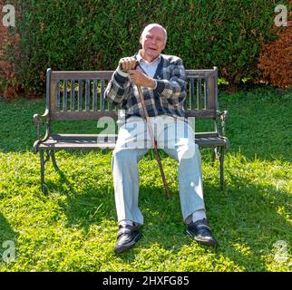 old man enjoys sitting on a bench in his garden Stock Photo