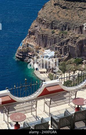 Amazing view from a restaurants terrace with a table and chairs over the old harbour and the Aegean Sea in Santorini Stock Photo