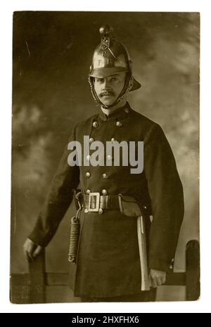 Original early 1900's postcard of handsome fireman in Eastbourne Fire Brigade  uniform - with an axe and rope attached to his belt, wearing a brass helmet, Studio of The Eastbourne Stereoscopic Co.,  U.K. circa 1915 Stock Photo