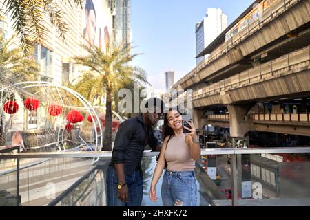 Asian woman and african man taking a selfie outside a mall Stock Photo