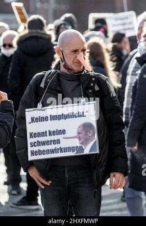 12 March 2022, Hamburg: A demonstrator with a Pinocchio nose carries a sign that reads 'No compulsory vaccination. Knows no serious side effects'. Critics of the stately health measures are demonstrating here under the slogan 'Against mandatory masks and other Corona containment measures' . Photo: Markus Scholz/dpa Stock Photo