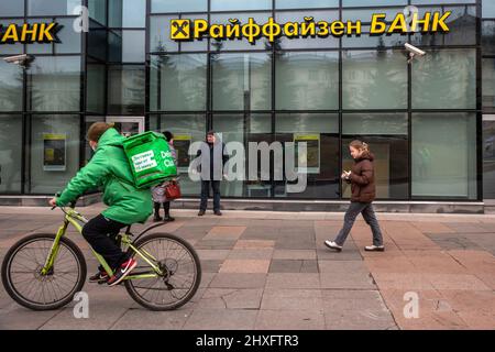 Moscow, Russia. 12th of March, 2022 A food delivery worker rides a bicycle outside view of a Raiffeisenbank branch at Leningradskoe shosse in Moscow, Russia Stock Photo