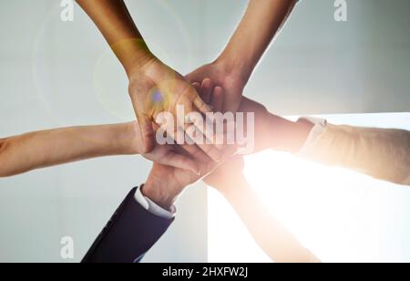 Share the goal, share the success. Low angle shot of a group of colleagues joining their hands in solidarity. Stock Photo