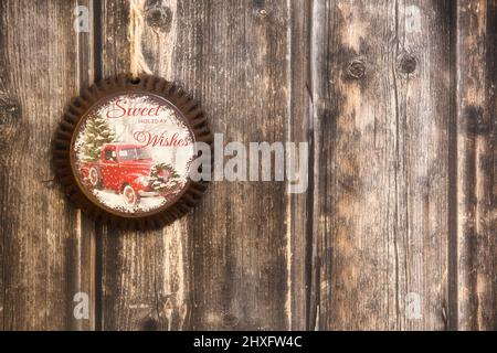 A vintage Christmas ornament made of steel with a truck on it hanging by twine from a weathered wood plank wall Stock Photo