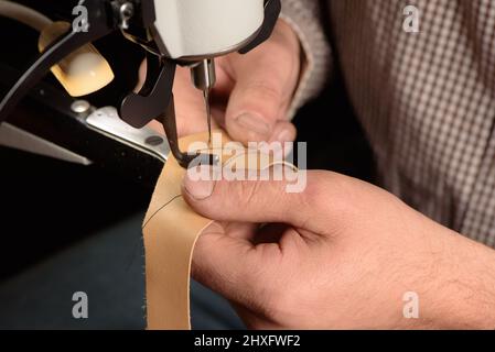 Industrial sewing machine in workshop of shoemaker. Bootmaker setting up professional sewing equipment on factory. Closeup of hands stitching leather. Stock Photo