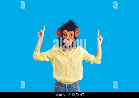 Woman wearing funny monkey mask pointing her index fingers up isolated on blue background Stock Photo