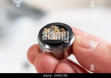A clogged dirty faucet aerator with calcium plaque in the hand of a plumber. Tap filter above the bathroom sink. Macro shot. Home maintenance concept. Stock Photo