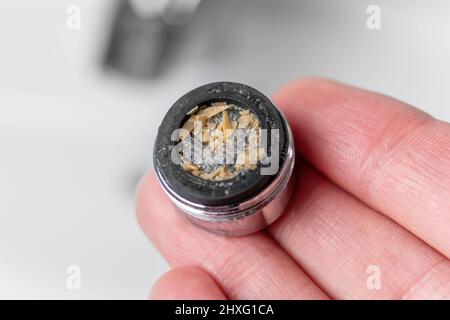 A clogged dirty faucet aerator with calcium plaque in the hand of a plumber. Tap filter above the bathroom sink. Macro shot. Home maintenance concept. Stock Photo