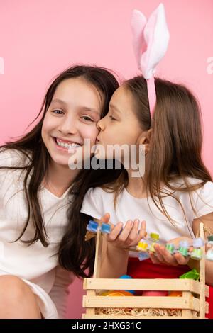Lovely photo of a pretty girl bunny ears on head kissing her smiling mother on the cheek and holding a box with paint for eggs. Easter concept holiday Stock Photo