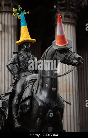 Glasgow, UK, 12th March 2022. Duke of Wellington statue in Queen Street wearing a blue and yellow Ukrainian-flag themed police cone hat, as crocheted by Pauline McWhirter, in support of Ukraine in their current war with President PutinÕs Russia, in Glasgow, Scotland, 12 March 2022. Photo credit: Jeremy Sutton-Hibbert/Alamy Live News. Stock Photo