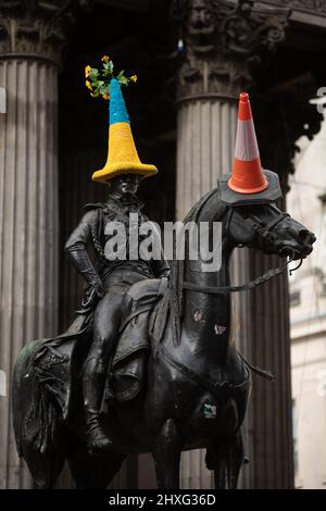 Glasgow, UK, 12th March 2022. Duke of Wellington statue in Queen Street wearing a blue and yellow Ukrainian-flag themed police cone hat, as crocheted by Pauline McWhirter, in support of Ukraine in their current war with President PutinÕs Russia, in Glasgow, Scotland, 12 March 2022. Photo credit: Jeremy Sutton-Hibbert/Alamy Live News. Stock Photo