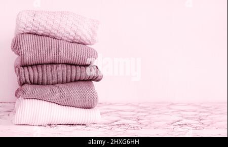 Stack of knitted pink warm sweaters on table Stock Photo