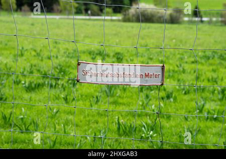Sign 'Sicherheitsabstand ein Meter' (safety distance one metre) on a chain-link fence. Stock Photo