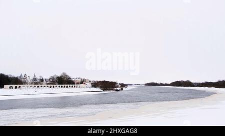 Flying over the winter river partially covered by ice and snow on cloudy sky background. Concept. Cold weather in a small town with bald trees. Stock Photo