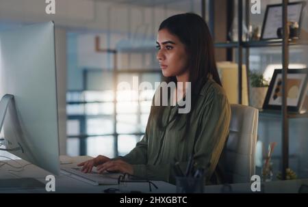 Putting in some extra effort towards her new project. Shot of a young businesswoman working on a computer in an office at night. Stock Photo