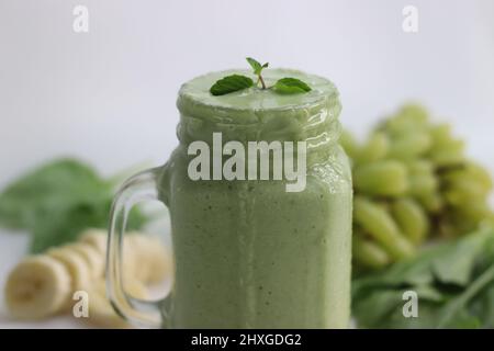 Green smoothie made of frozen green grapes, fresh baby spinach, bananas and almond milk. Served in mason jar. Shot on white background. Stock Photo