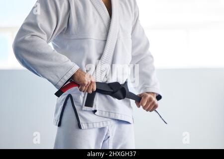Hes an expert. Cropped shot of an unrecognizable male martial artist tying his belt in the gym. Stock Photo