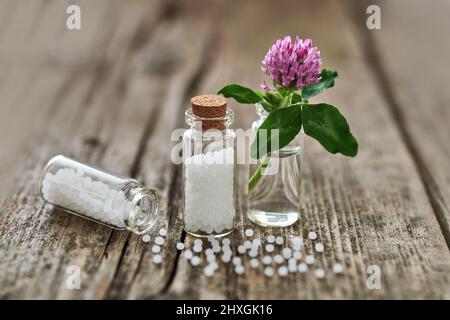 Homeopathic granules in small glass flasks, some granules scattered on the old wooden table and a small flower. Stock Photo