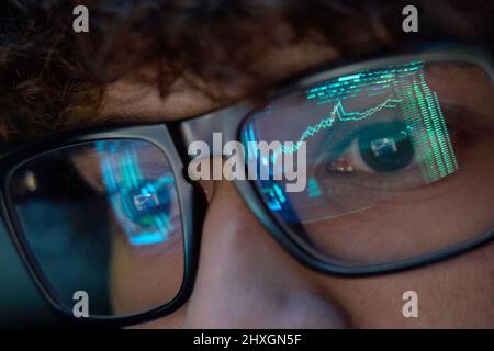 Young business man looking at trading charts reflecting in glasses, close up. Stock Photo