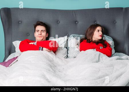 Young couple lying in bed, looking angry with each other. Relationship problems Stock Photo
