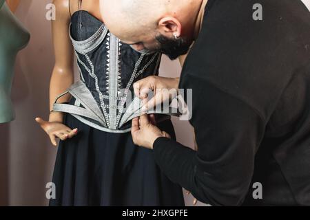 Close up photo of fashion designer working on his new creation. Using needle to sew fabric on top part of the dress. Fashion design concept Stock Photo