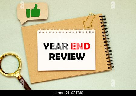 Top view of pen,sunglasses,a cup of coffee and notebook written with Year End Review on wooden background. Stock Photo