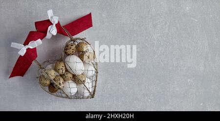 Chicken and quail eggs in a heart shaped woven metal wire basket Stock Photo