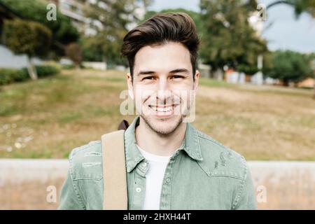 Trendy handsome young student man with backpack smiling at camera Stock Photo