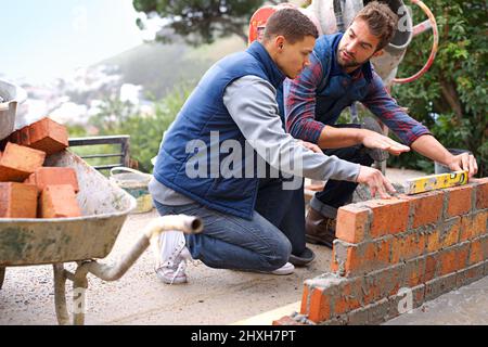 Making strong foundations - Teaching the basics. Shot of bricklayers at work. Stock Photo