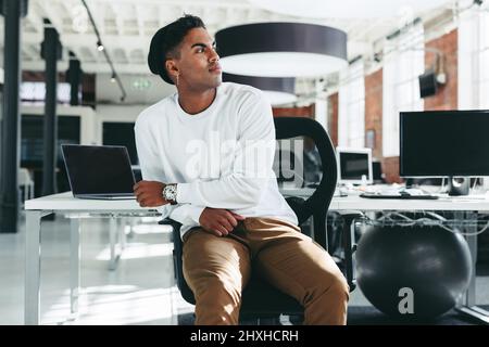 Thinking of new software ideas. Creative businessman looking away thoughtfully while sitting alone in a modern workplace. Young software developer tak Stock Photo