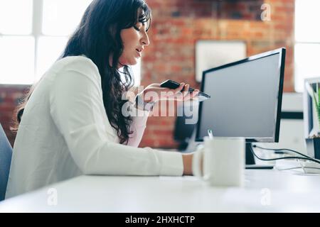 Contacting business clients in the office. Focused young businesswoman making an important phone call while sitting in a modern office. Young business Stock Photo