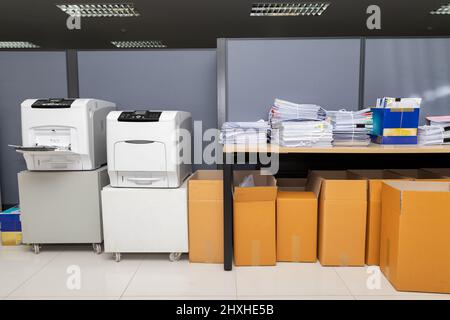 Printers, business documents stack on desk and cardboard boxes under desk. Stock Photo