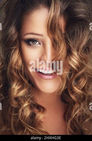 Your hair is your best accessory. Cropped shot of a beautiful woman with long brown curls posing against a grey background. Stock Photo
