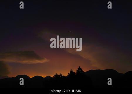 Sunset panoramic view from top of mountain peak with yellow moon silhouette on background of sky gradient at dusk Stock Photo