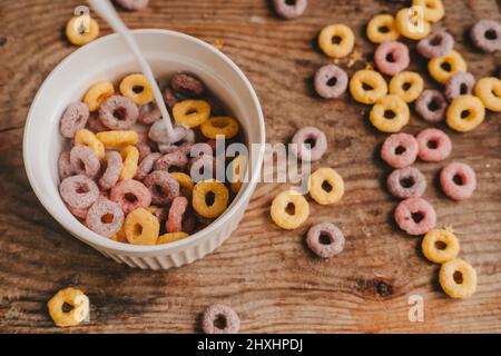 pouring milk into colorful round fruit flakes in white bowl scattered on brown wooden table Stock Photo