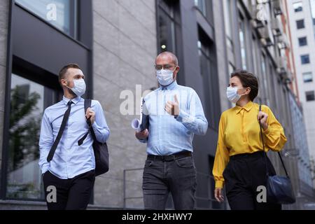Business or finance industry concept. Managers team in medical masks going down the street in city downtown and discussing project presentation, talking or brainstorming. High quality image Stock Photo
