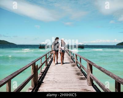 We are finally on holiday. Shot of a carefree young couple walking on a jetty together next to the ocean during the day. Stock Photo