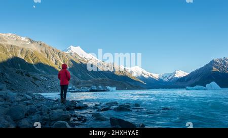Tourist standing on the shore of Tasman Glacier terminal lake looking at snow-capped mountains and icebergs Stock Photo