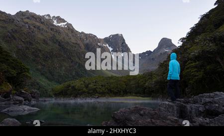 A tramper standing on the rocks by the Lake Mackenzie at dawn, Routeburn Track, one of the great walks of New Zealand. Stock Photo
