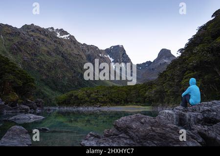 A tramper sitting on the rocks by the Lake Mackenzie at dawn, Routeburn Track, South Island Stock Photo