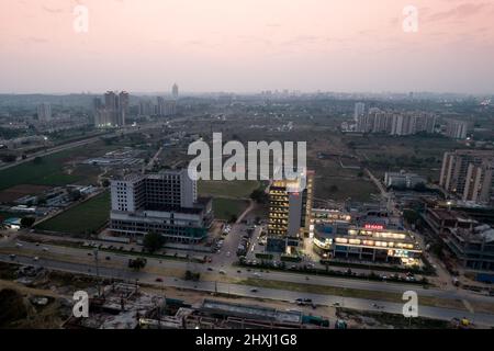 aerial dusk shot showing the 3 road shopping mall lit up with the under construction buildings around it unlit as the sun sets Stock Photo