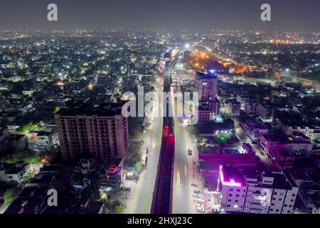 aerial drone shot showing elevated metro track over lit road surrounded by densely populated buildings with homes shops and skyscrapers Stock Photo